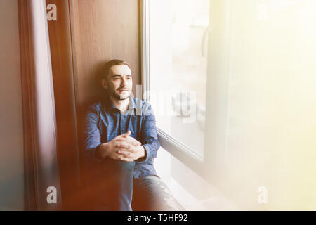 Handsome young man sitting on windowsill Stock Photo