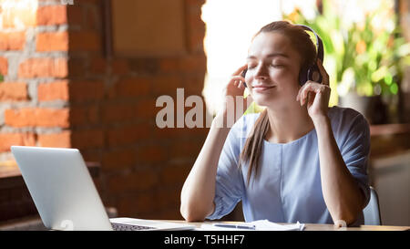 Young woman wearing headphones listening favourite music sitting indoors