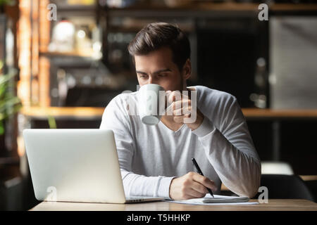 Serious businessman sitting in coffeehouse drinking coffee looking at computer Stock Photo