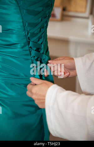 Bridesmaid dress being done up from behind in close up, teal green dress being laced up before the wedding ceremony Stock Photo