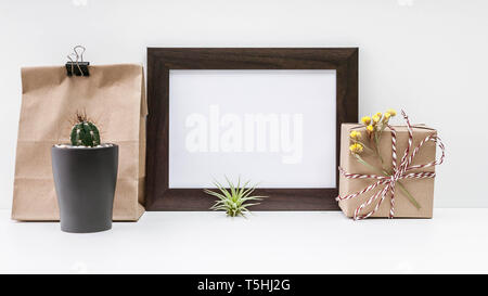 Mock dark photo frame, cactus, paper bag, gift box in paper packaging on a light background. Stock Photo