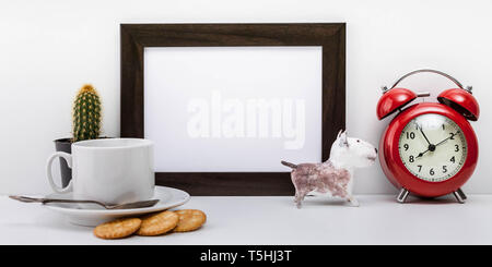 Mock Up dark photo frame, red alarm clock, dog figure, crackers and white cup of coffee with saucer on a light background. Scandinavian style Stock Photo