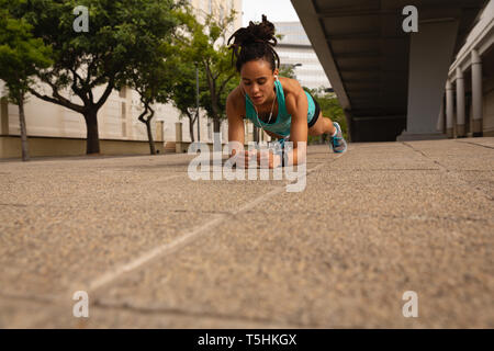 Woman listening music on earphones while doing plank exercise in the city Stock Photo