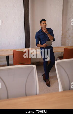 Thoughtful businessman standing in office with digital tablet Stock Photo