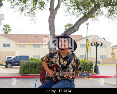 A handsome young man with dark complexion in a black, wide-brimmed hat plays an electric guitar at the Corpus Christi Southside Farmers' Market. Stock Photo