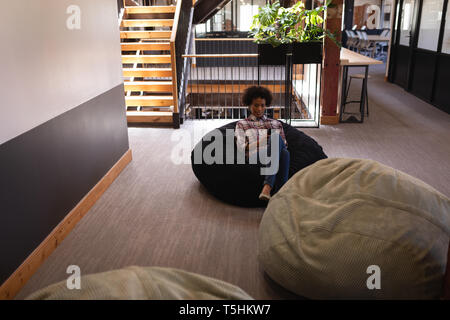 Businesswoman using mobile phone while relaxing at bean bag Stock Photo