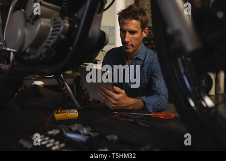 Bike mechanic using digital tablet while working in garage Stock Photo