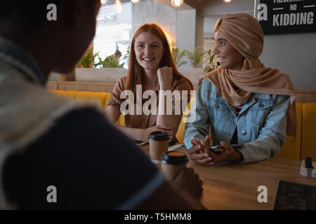 Female friends interacting with each other while having coffee Stock Photo