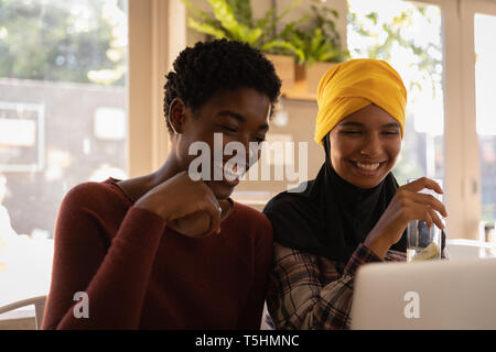 Female friends interacting with each other while using laptop Stock Photo