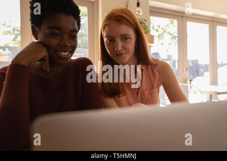 Female friends interacting with each other while using laptop Stock Photo