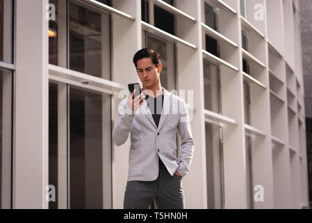Handsome man using mobile phone while standing near building Stock Photo