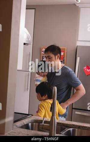 Father holding his children while talking with them in kitchen Stock Photo