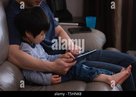 Father and son using digital tablet while sitting on sofa Stock Photo