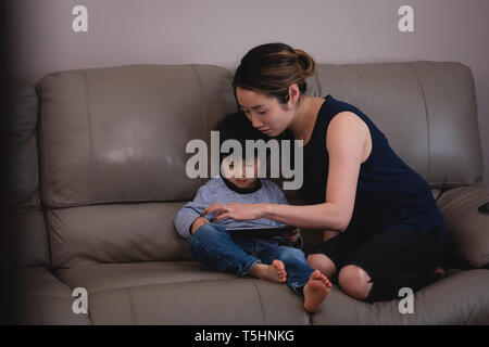 Mother and son using digital tablet while sitting on sofa at home Stock Photo