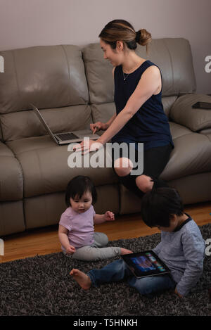 Mother using laptop while kids playing on rug at home Stock Photo