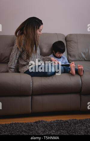 Mother and son using digital tablet while sitting on sofa at home Stock Photo