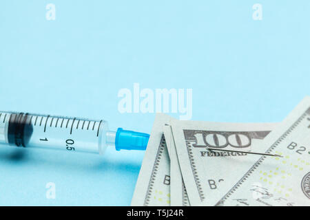 Syringe and paper dollars pinned to needle on blue background. Expensive medical insurance. Copy space for text Stock Photo