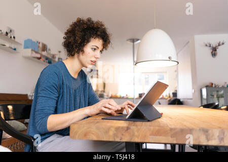 Young woman sitting at table, using digital tablet Stock Photo