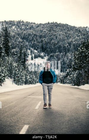 Young man walking on a snowy road with trees in the background Stock Photo