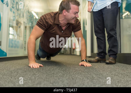 Businessman doing push-ups on office floor Stock Photo