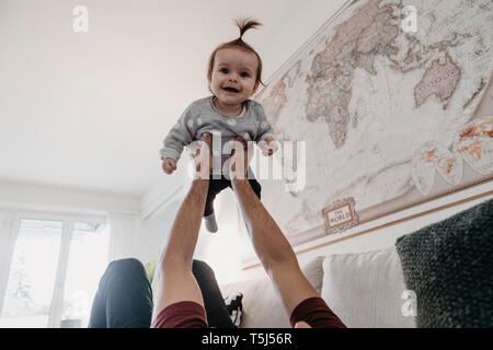 Happy baby girl being lifted up by her father in living room at home Stock Photo