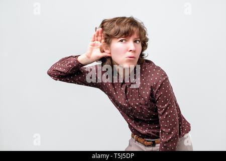 Woman with curly hair placing hand on her ear, listening attentively, trying to overhear Stock Photo