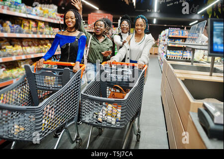 Group of five african womans walking and having fun together in supermarket with shopping carts. Stock Photo