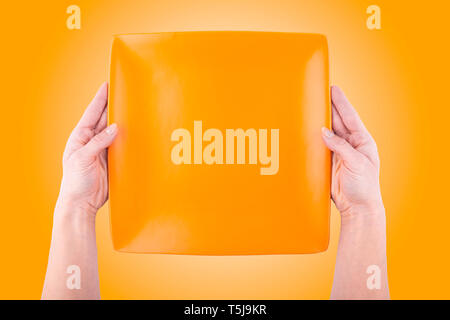 Female hands holding orange square empty plate over orange background top view - Two woman hands holds empty dish flat lay isolated Stock Photo