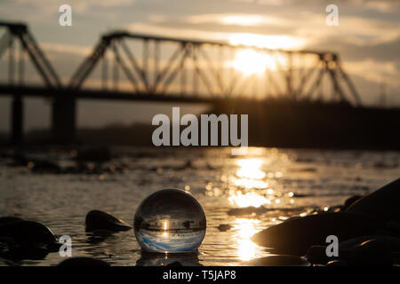 Sunset captured through a lens ball, with river in the foreground and a train bridge in the background. Stock Photo