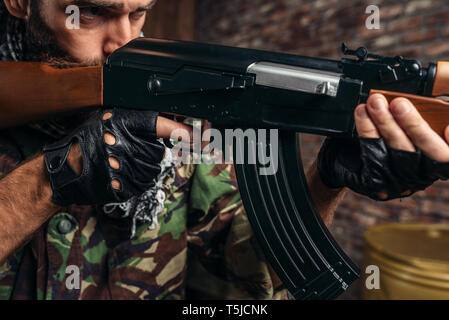 Cruel terrorist in uniform aiming from a kalashnikov rifle closeup, man with weapon. Terrorism and terror concept Stock Photo