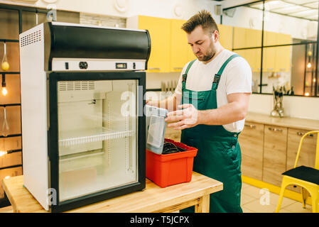 Worker with toolbox repair refrigerator at home. Repairing of fridge occupation, professional technical service Stock Photo