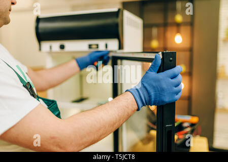 Repairman in uniform repairs refrigerator at home. Repairing of fridge occupation, professional service Stock Photo