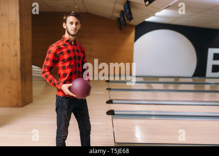 Male bowler standing on lane and holds ball in hands, back view. Bowling alley player poses in club, active leisure Stock Photo