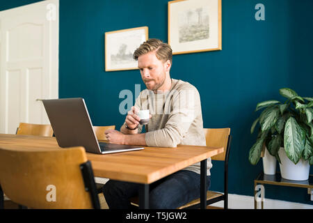 Man working on laptop on wooden table in home office drinking espresso Stock Photo