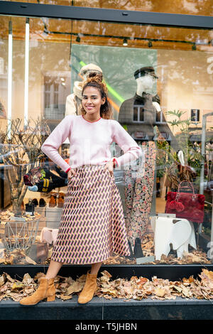 Young woman standing in front of fashion store, with hands on hips Stock Photo