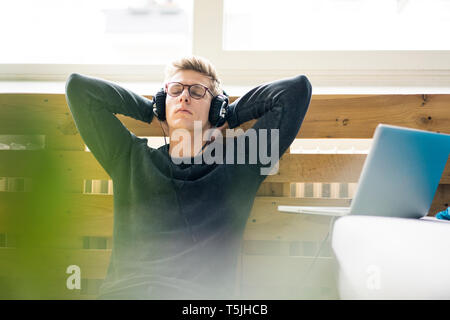 Relaxed young man sitting on the floor listening to music with headphones Stock Photo