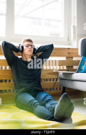 Relaxed young man sitting on the floor listening to music with headphones Stock Photo