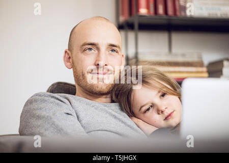 Father and daughter sitting on couch, using laptop Stock Photo