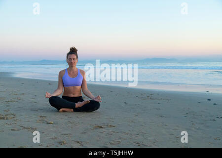 Woman meditating on the beach in the evening Stock Photo