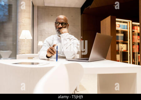 Portrait of pensive man sitting at library in the evening Stock Photo