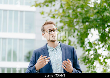 Young businessman standing in front of modern office building, talking Stock Photo