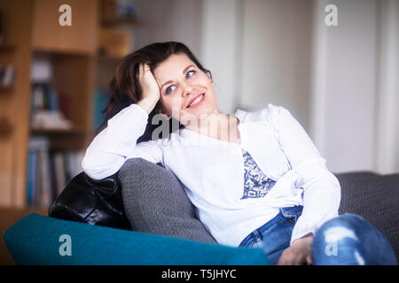 Portrait of smiling young woman sitting on couch at home relaxing Stock Photo