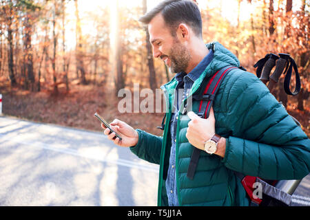 Smiling man checking smartphone on a road in the woods during backpacking trip Stock Photo