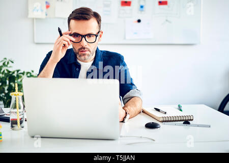 Casual businessman working on laptop at desk in office Stock Photo