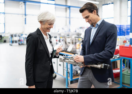 Smiling businessman and senior businesswoman examining workpiece in a factory Stock Photo