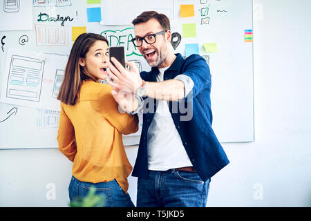 Excited colleagues looking at smartphone in office Stock Photo