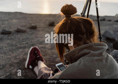 Spain, Canary Islands, Fuerteventura, young woman using smartphone and digital camera Stock Photo