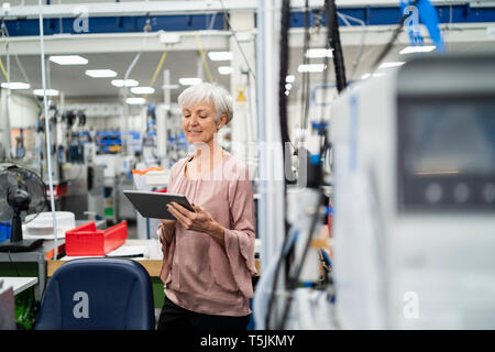Smiling senior woman using tablet in a factory Stock Photo
