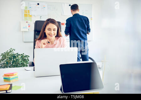 Woman working at desk in office with colleague in background Stock Photo