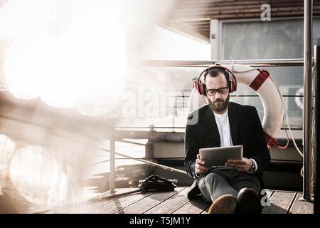 Hip businessman working on a houseboat, using headphones and digital tablet Stock Photo